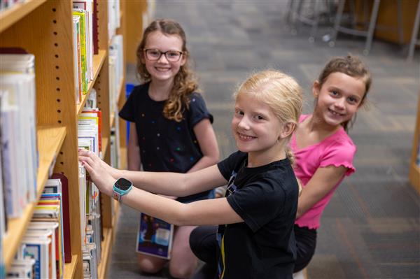 three girls smiling next to bookshelf